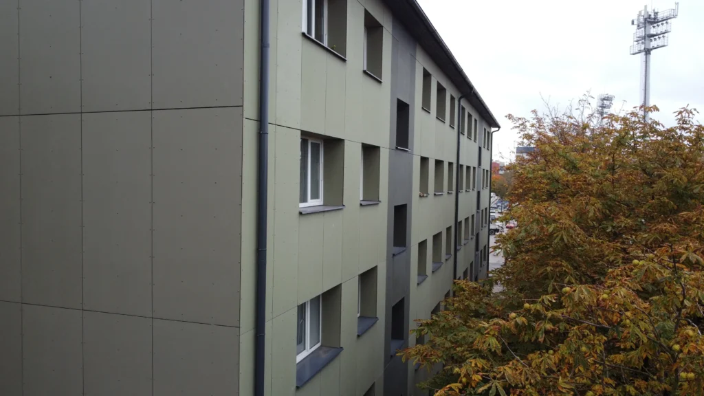 Side facade of an apartment building in an olive-grey tone with rows of windows.