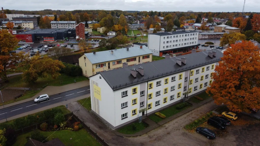 Renovēta 3 stāvu daudzdzīvokļu māja ar baltu fasādi, dzelteniem akcentiem un melnu slīpu jumtu