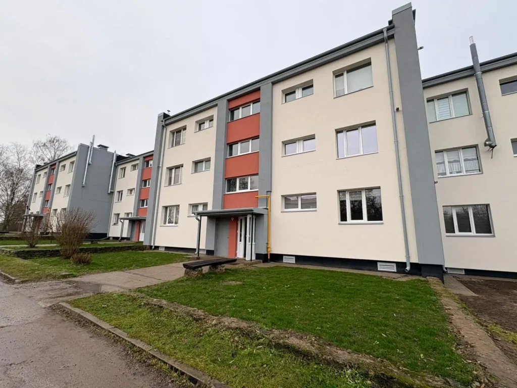 4-storey apartment building with a white facade, red accents and grey corners near the entrance.