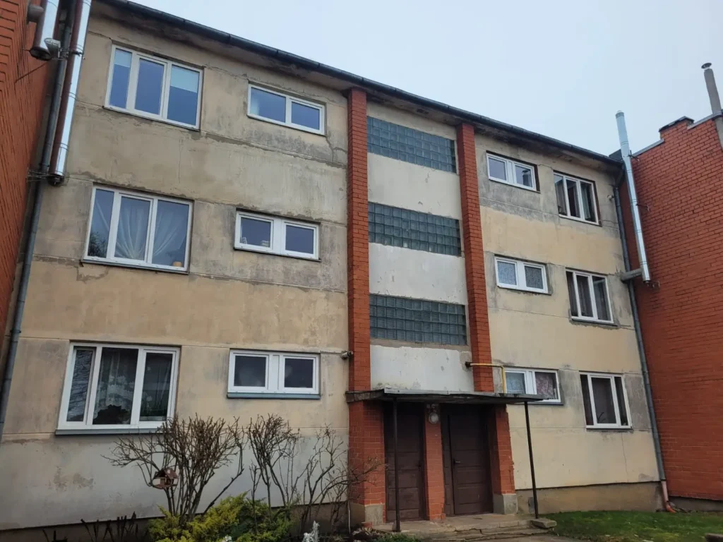 Apartment building before renovation with a beige facade and an entrance section between brick walls.