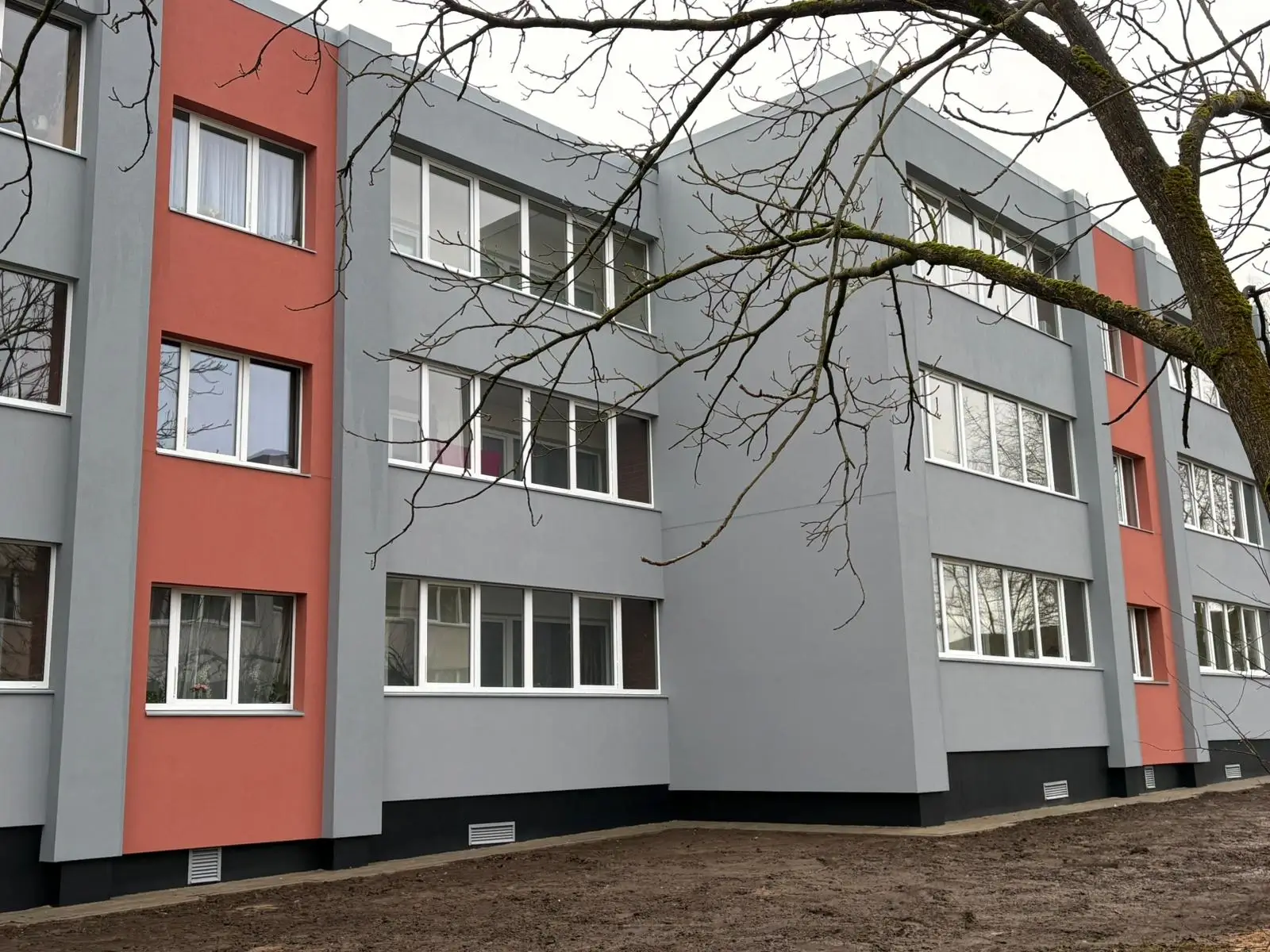 3-storey apartment building with a grey facade and a red band.