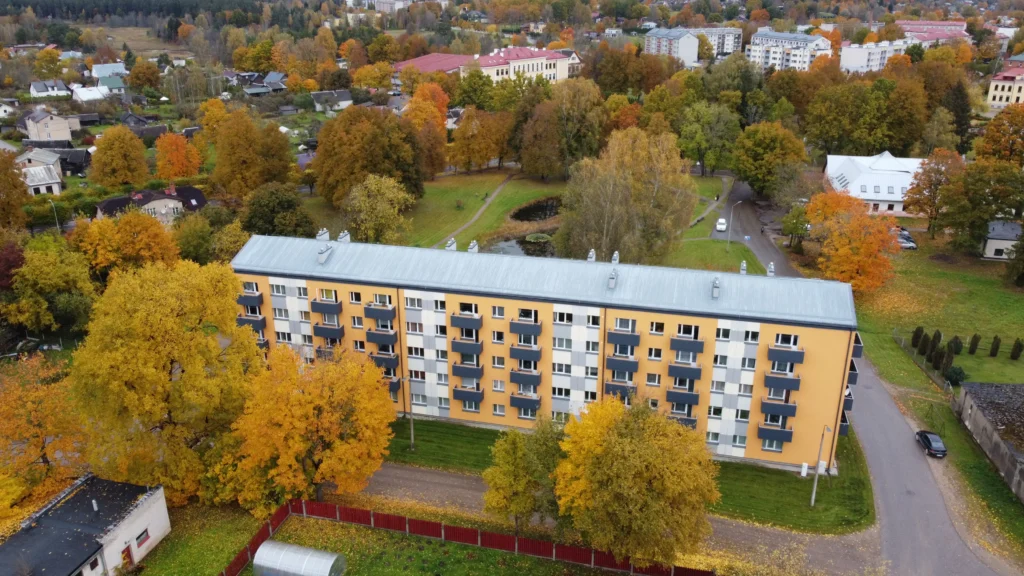 5 stāvu daudzdzīvokļu ēka ar oranži baltu fasādes apdari, tumšiem balkoniem un pelēku jumtu
