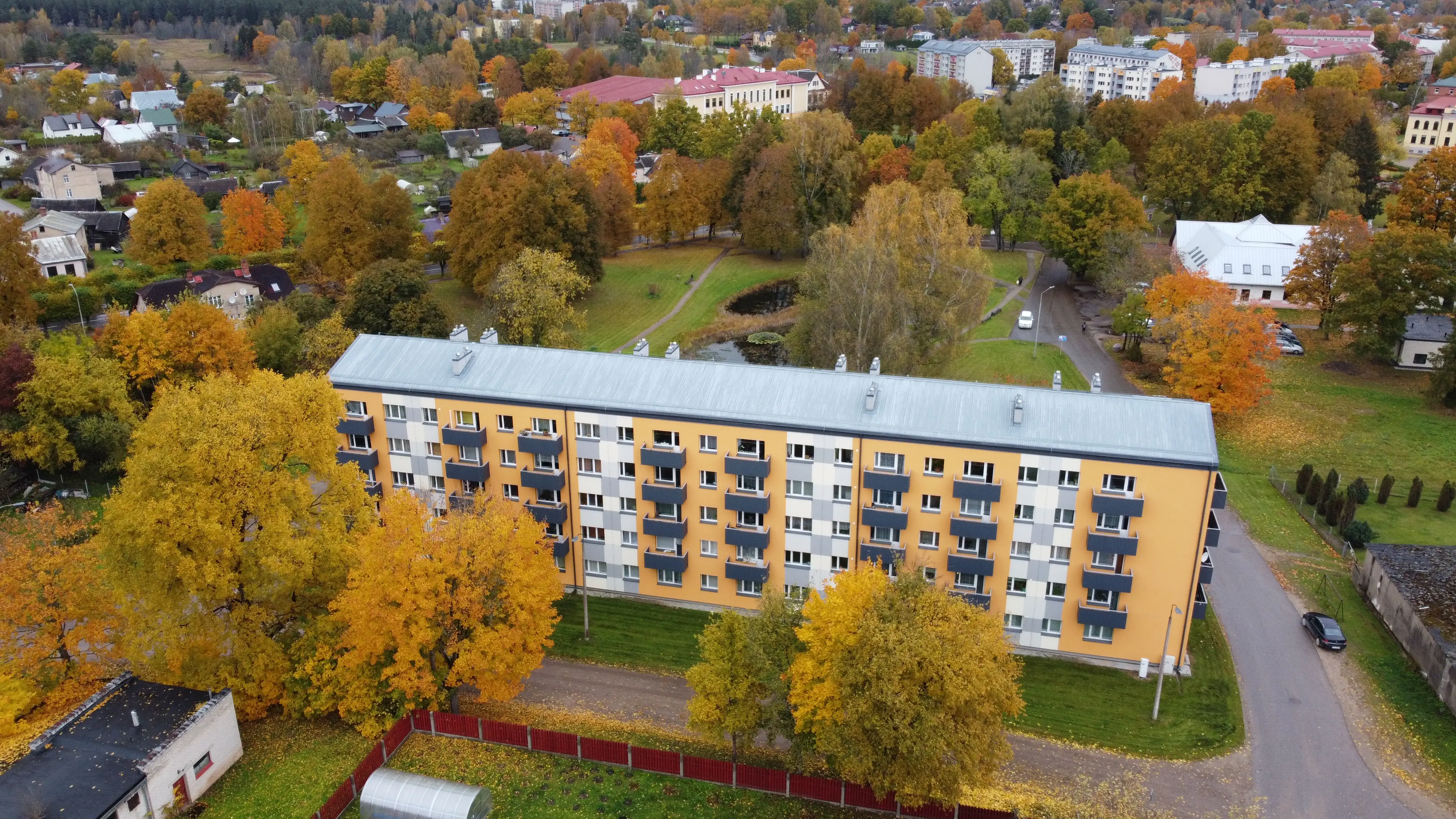 5 stāvu daudzdzīvokļu ēka ar oranži baltu fasādes apdari, tumšiem balkoniem un pelēku jumtu