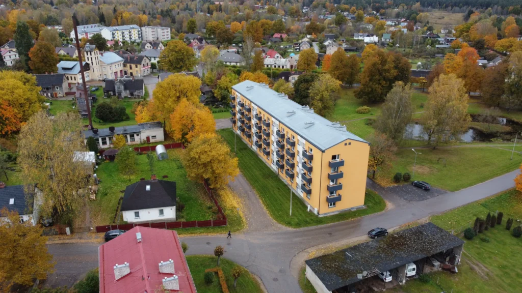 5 stāvu daudzdzīvokļu ēka ar oranžu fasādes apdari, melniem balkoniem un pelēku jumtu