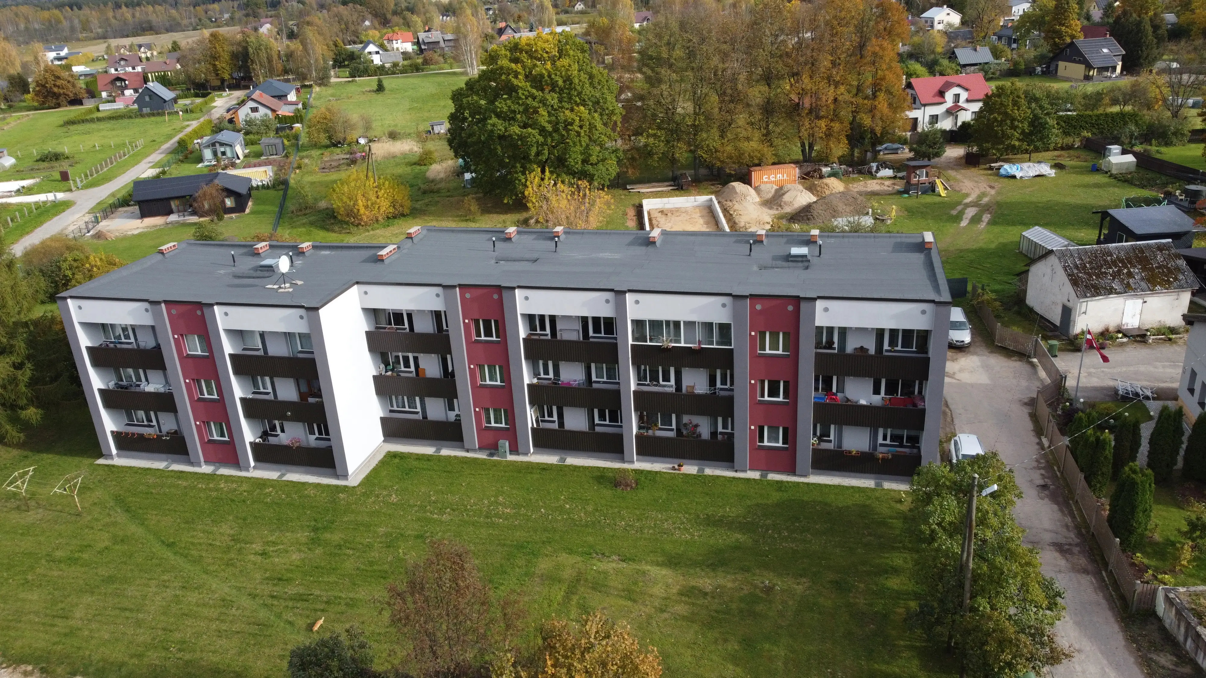 4 stāvu daudzdzīvokļu ēka ar pelēkbaltu fasādes apdari, sarkanām vertikālām joslām un balkoniem, Valka