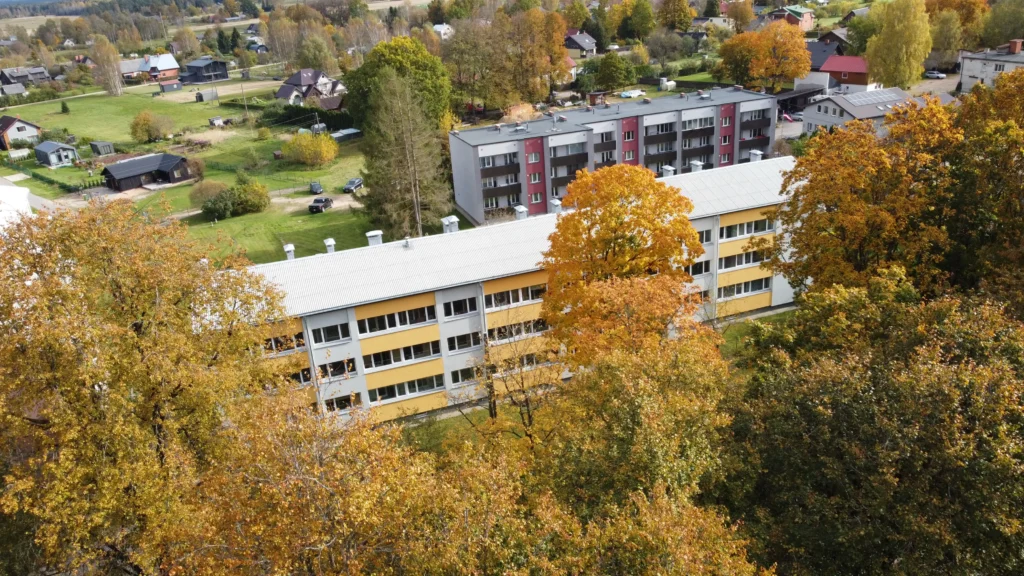 Daudzdzīvokļu ēkas ar baltu un dzeltenu fasādes apdari un pelēku jumtu, fonā piecstāvu nams ar sarkaniem fasādes akcentiem