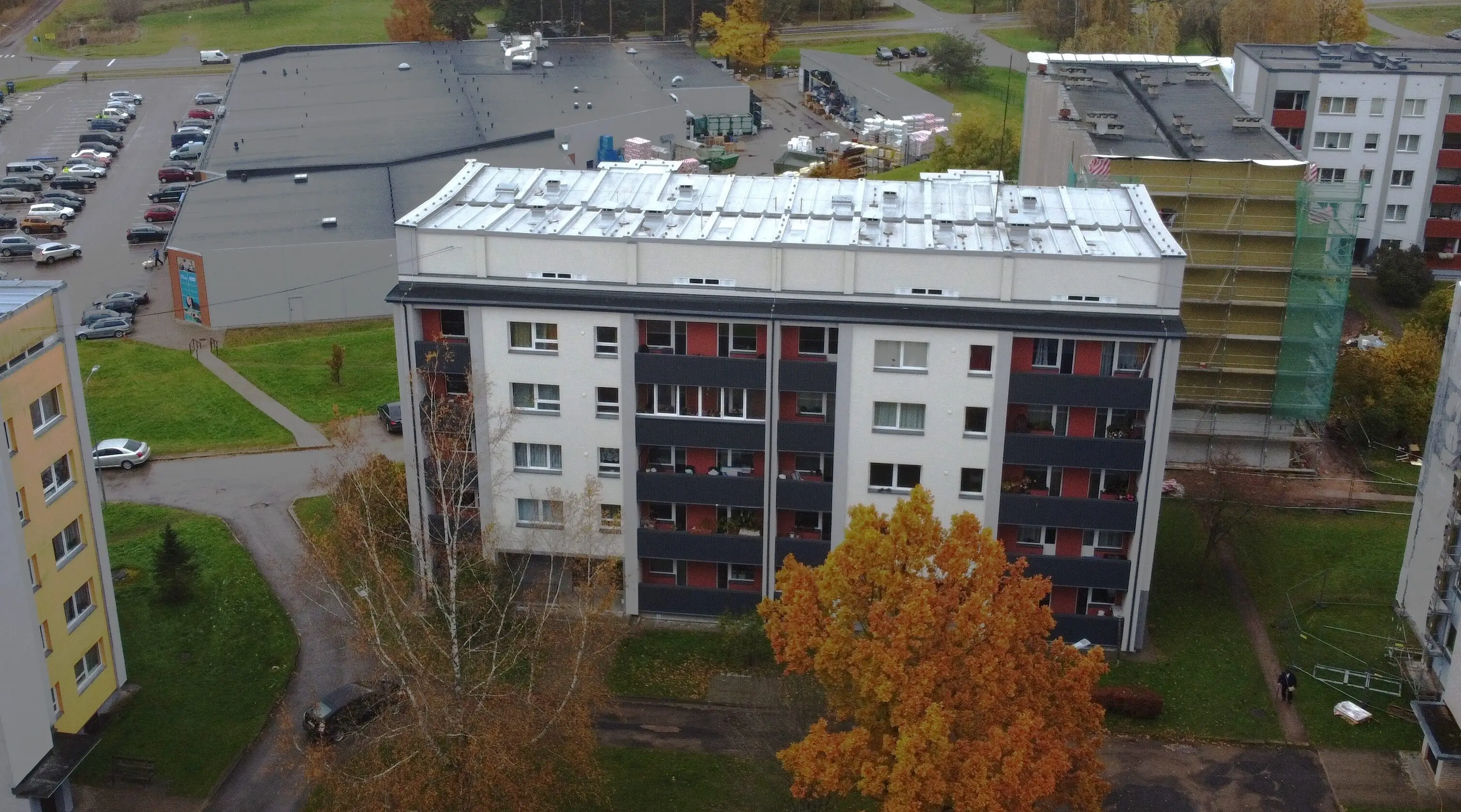 5 stāvu daudzdzīvokļu ēka ar gaišu fasādi, tumšiem balkoniem un pelēku jumtu.