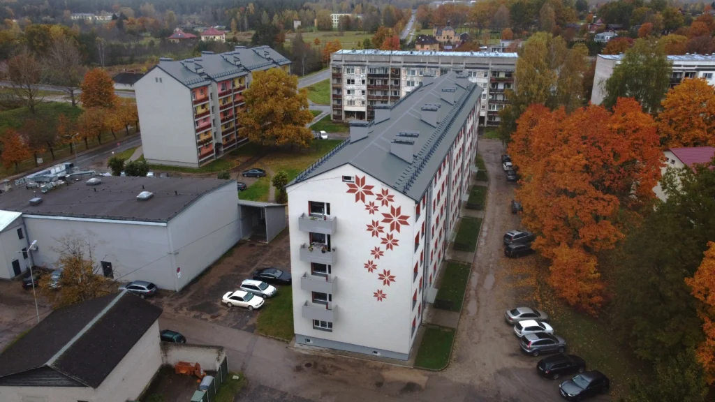 5 stāvu daudzdzīvokļu ēka ar baltu fasādes apdari, dekoratīviem sarkaniem rakstiem un pelēku jumtu, Valka