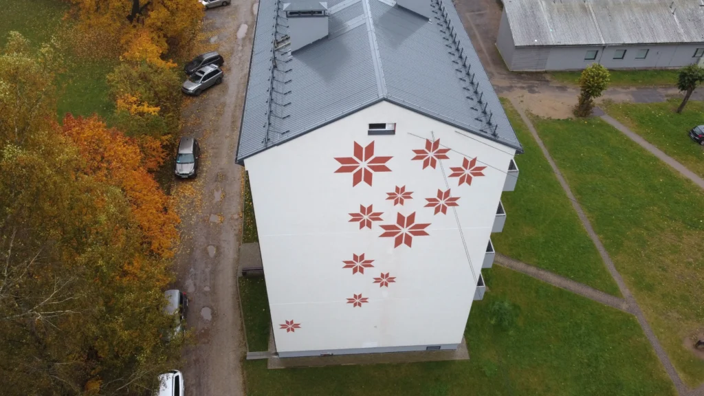 Dekoratīvi sarkani raksti uz baltas fasādes daudzdzīvokļu ēkas gala sienas, Valka