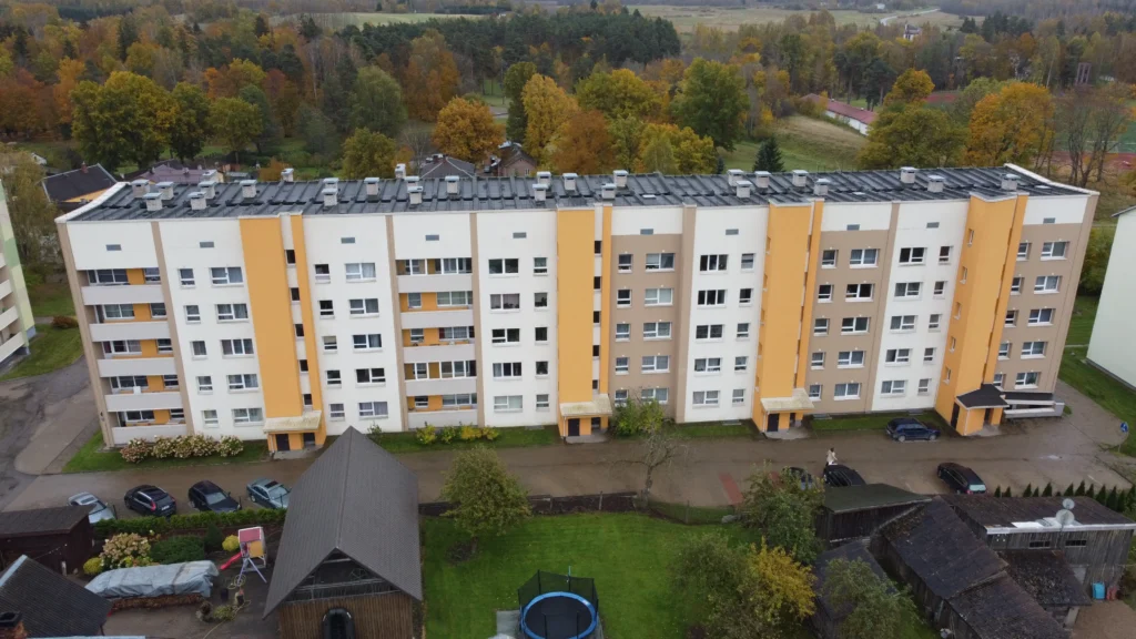 daudzdzīvokļu māja ar atjaunotu fasādi un dzelteniem akcentiem, drona skats uz pagalmu