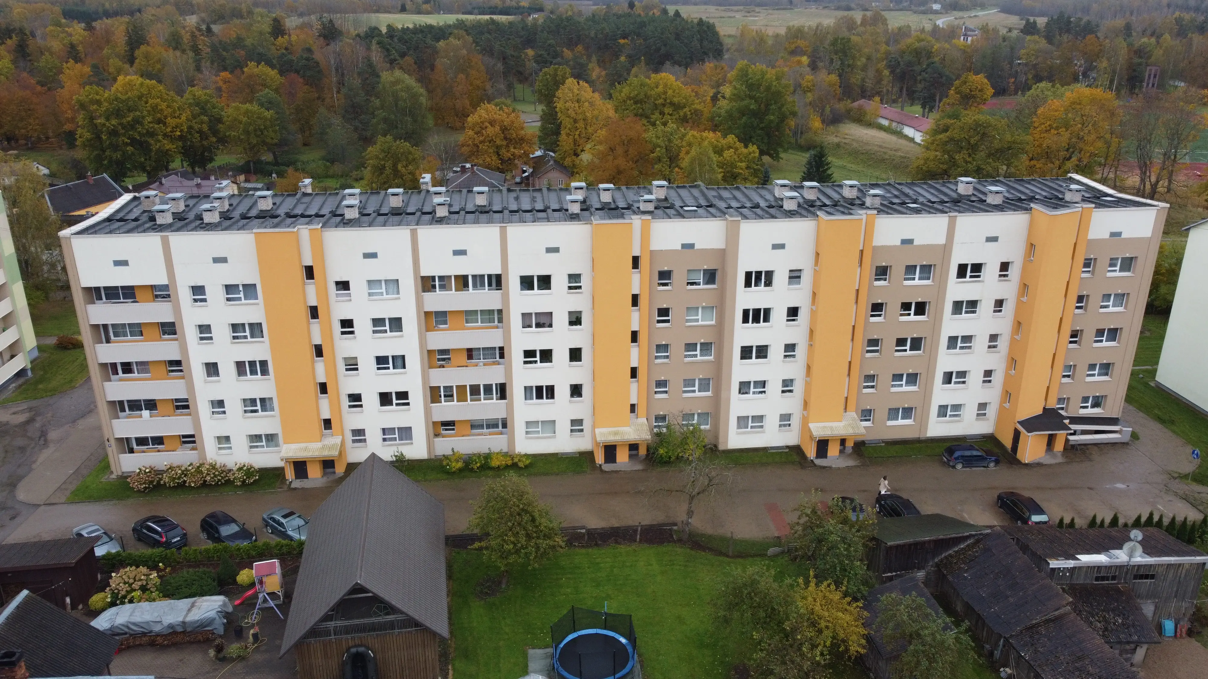 daudzdzīvokļu māja ar atjaunotu fasādi un dzelteniem akcentiem, drona skats uz pagalmu