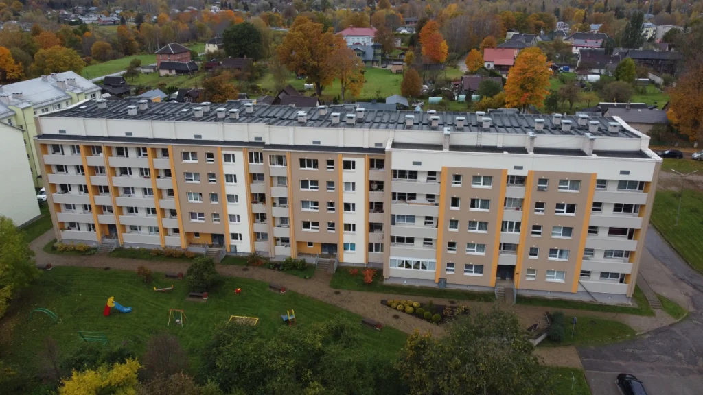 Daudzdzīvokļu māja ar bēšu un gaišu fasādi, drona skats uz pagalmu ar bērnu laukumu