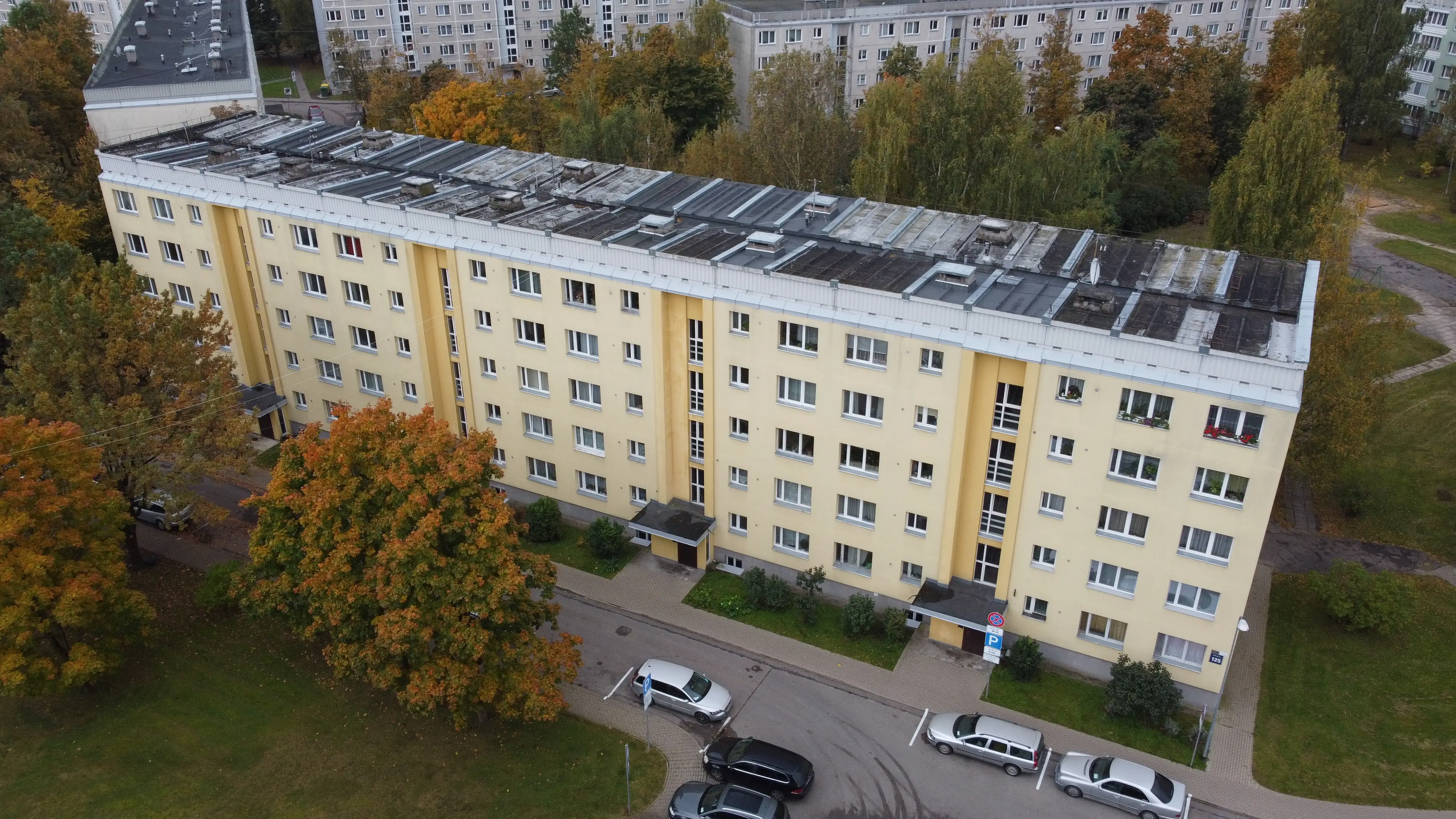 5 stāvu daudzdzīvokļu ēka ar gaiši dzeltenu fasādi un plakanu jumtu, pie ieejām stāvvieta un apzaļumota teritorija, Rīga