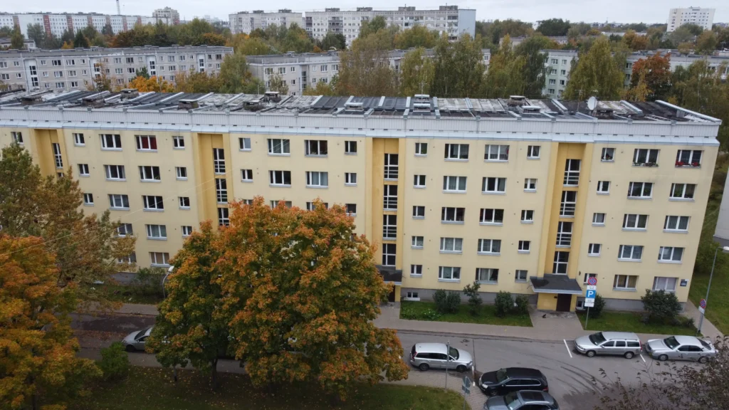 Renovēta 5 stāvu daudzdzīvokļu ēka ar dzeltenu fasādi, baltiem logiem un melnu plakano jumtu