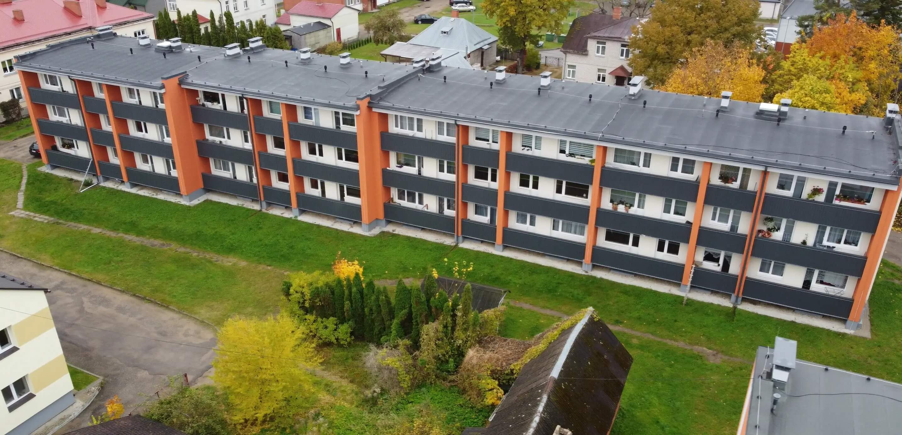 Apartment building with a white facade, orange accents, dark balconies and a dark flat roof.