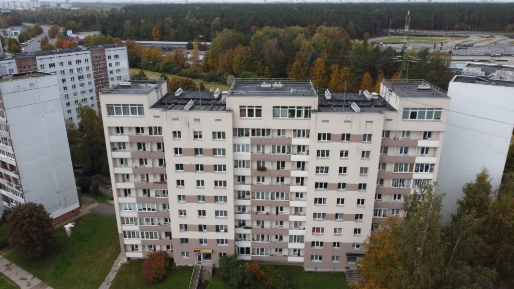 9 stāvu daudzdzīvokļu ēka ar gaiši bēšu fasādi, horizontālām lodžiju joslām un tumšu plakanu jumtu.