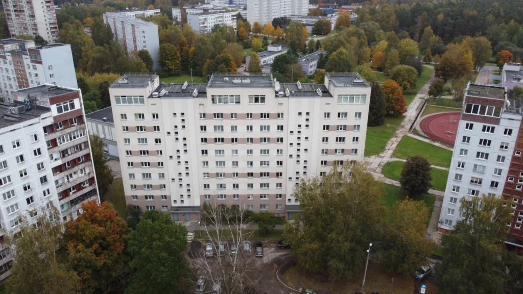 9 stāvu daudzdzīvokļu ēka ar gaiši bēšu fasādi, horizontālām lodžiju joslām un tumšu plakanu jumtu.