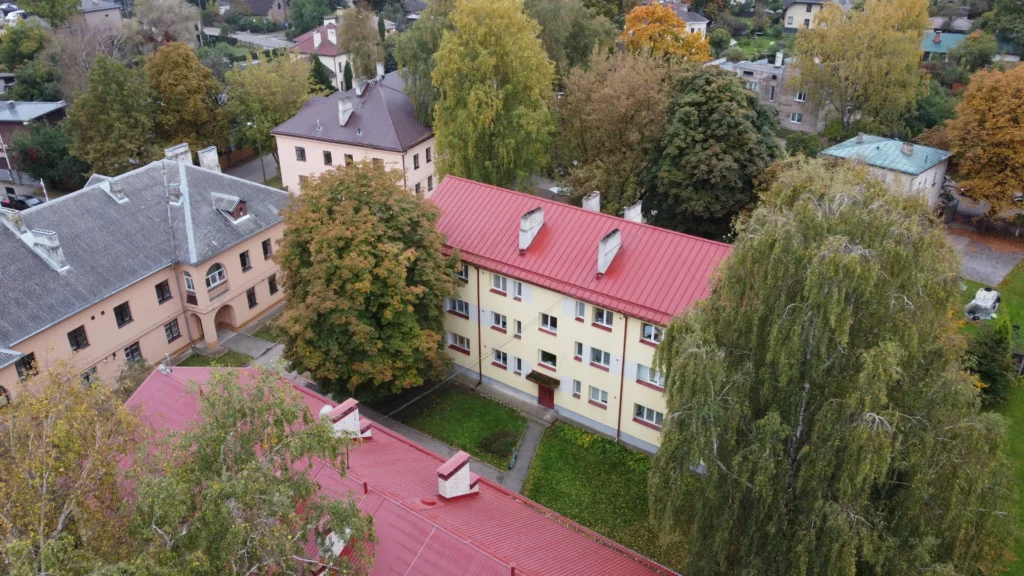 Trīsstāvu daudzdzīvokļu nams ar krēmkrāsas fasādi un sarkanu skārda jumtu, Rīga