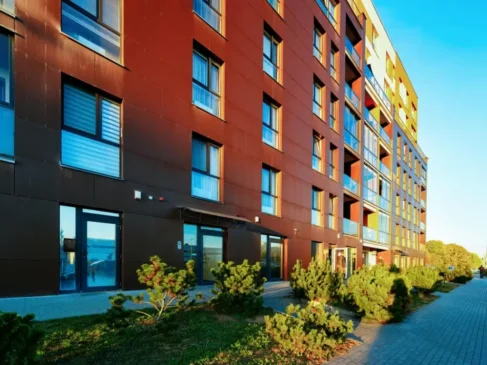 Modern apartment building facade with brown cladding, balconies and landscaping along a walkway