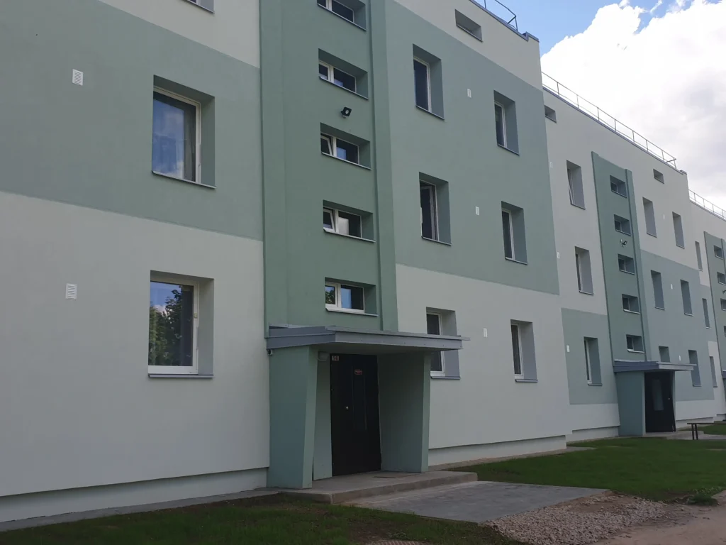 Apartment building facade in green tones with an entrance canopy and rows of windows.