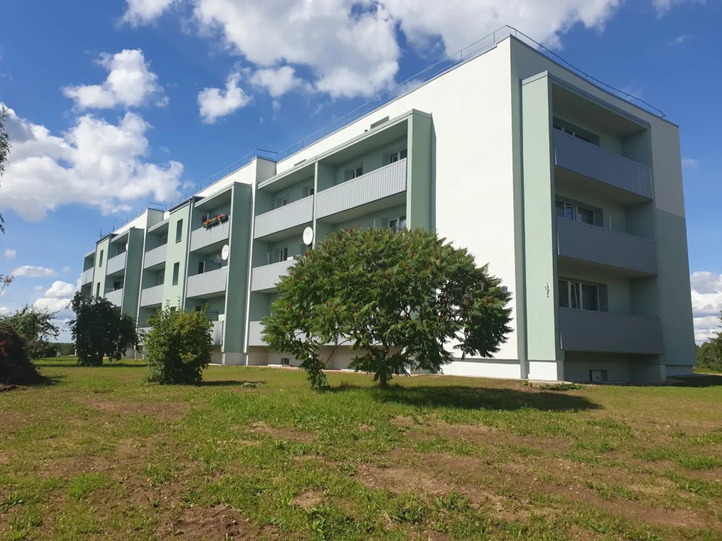Apartment building with light green facade finishing, grey balconies and a flat roof