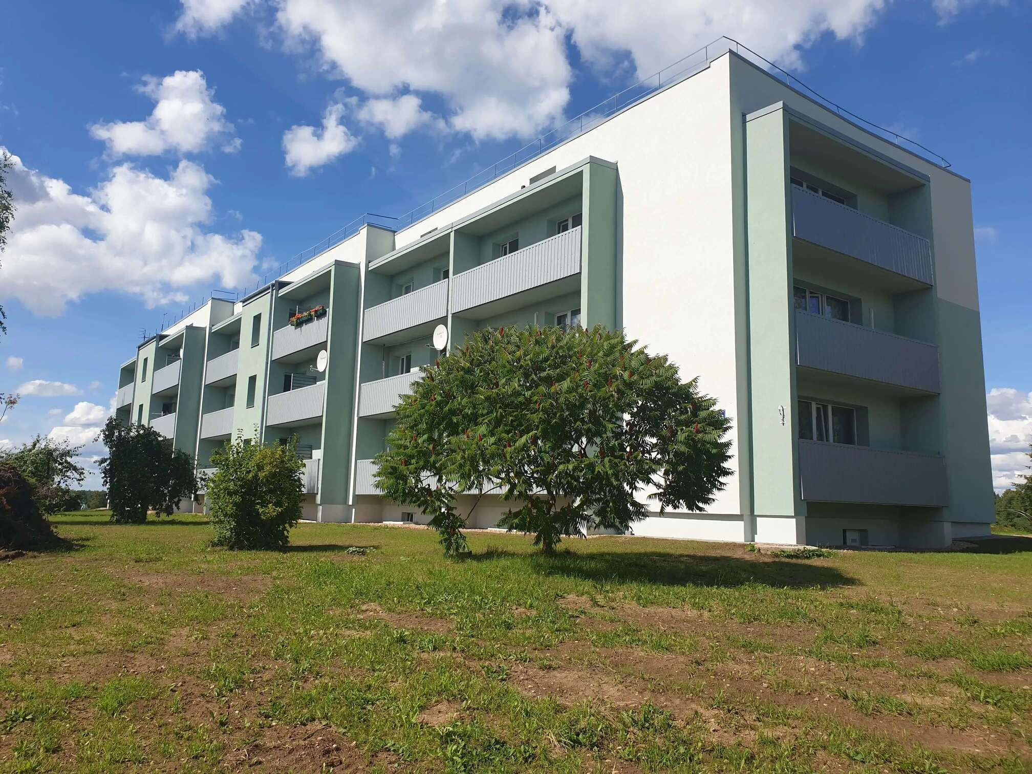 Apartment building with light green facade finishing, grey balconies and a flat roof