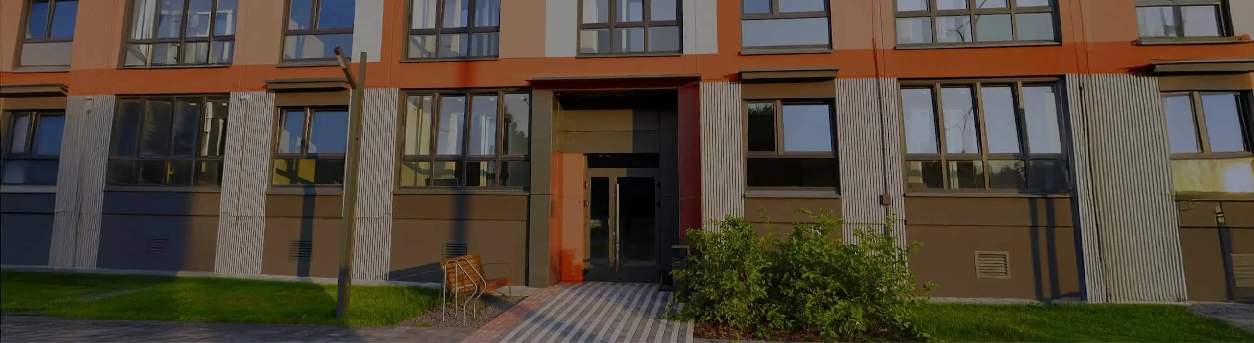 Modern apartment building with an orange facade and a main entrance with glass doors.