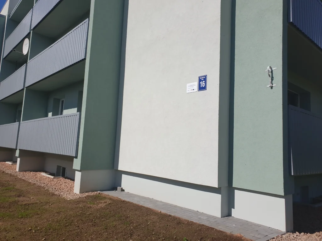 Corner of a renovated apartment building with a white facade, green accents and grey balconies.